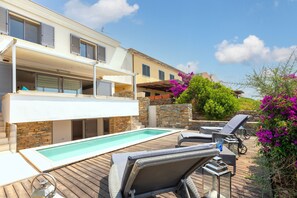 Un área junto a la piscina con sillas de descanso, piscina y un edificio con balcones.