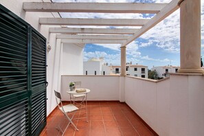 Ein Balkon mit weißem Tisch und Stühlen, einem grünen Tor und Blick auf Gebäude unter blauem Himmel.