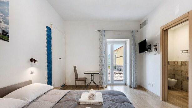Ein Schlafzimmer mit Bett, Stuhl, Tisch und einem durchgegangenen Tür sichtbaren Badezimmer.