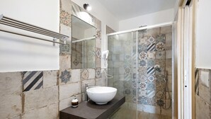 Ein Badezimmer mit einem großen, weißen Waschbecken, einem Handhaartrockner und einer Dusche mit gemusterten Fliesen.