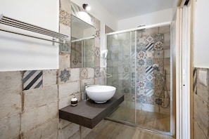 A bathroom with a large white vessel sink, a handheld hair dryer, and a shower with patterned tiles.