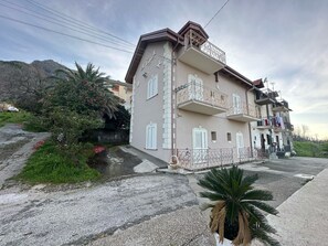 Un edificio de varios pisos con balcones, un jardín con plantas y un sendero pavimentado.