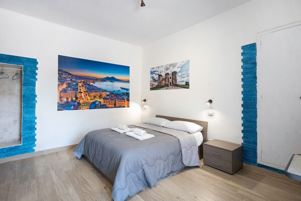 Un dormitorio con cama, dos lámparas de pared, una mesita de noche y dos cuadros.