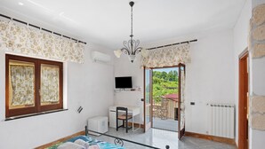 A bedroom with a bed, a desk, a chair, a TV, and a view of the outdoors. - Room 'Tripla Con Vista Vesuvio' with Mountain View, Wi-Fi and Air Conditioning (Pimonte)