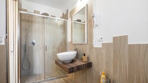 Ein modernes Badezimmer mit einer Duschkabine aus Glas, einem Holzkosmetikschrank mit weißem Waschbecken und einem Spiegel.