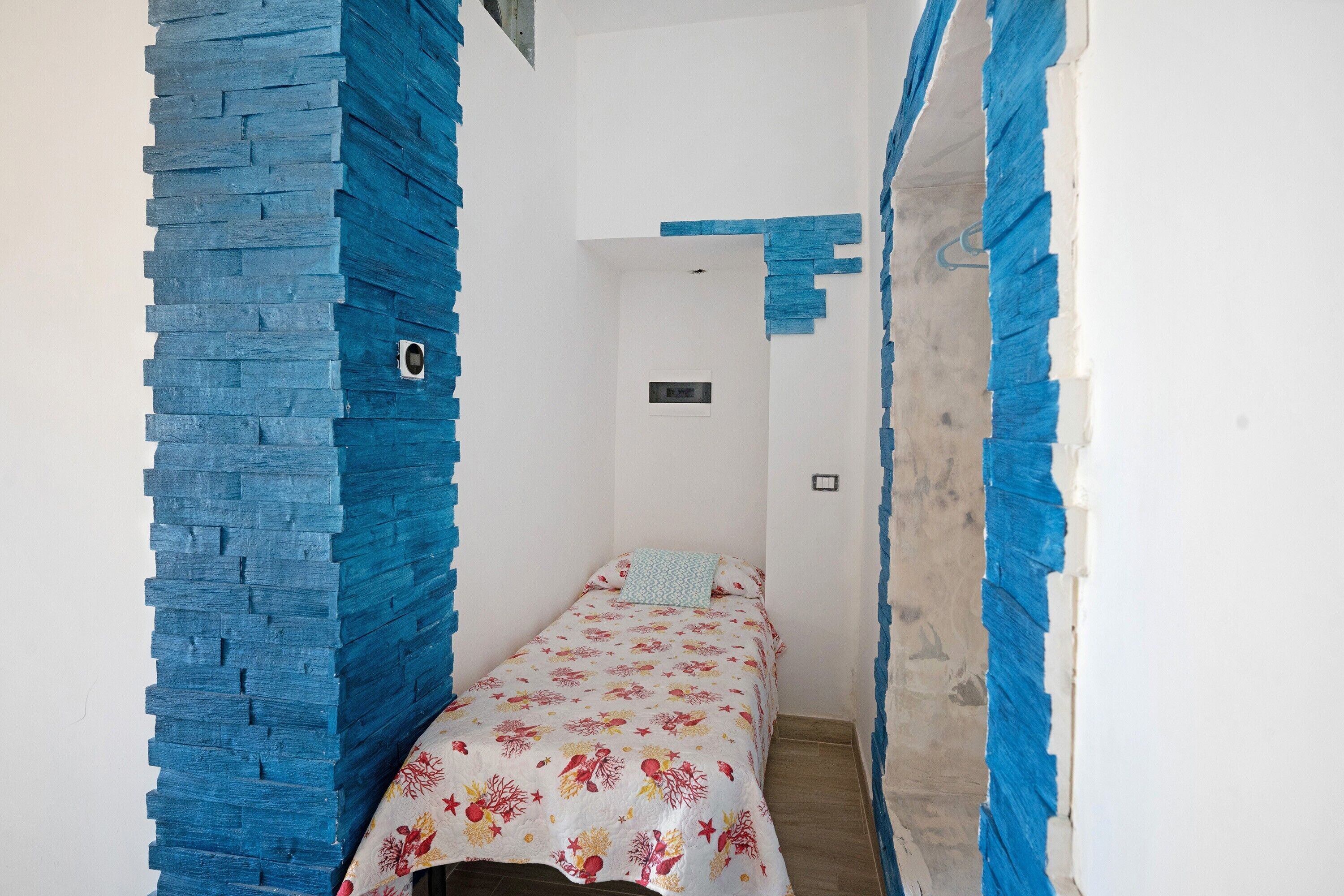 A narrow room with a bed, a wall-mounted light, and a door.