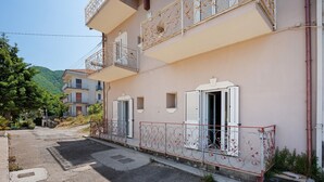 Un edificio de varios pisos con balcones, una calle pavimentada y una montaña al fondo.