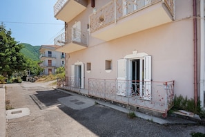 Un immeuble à plusieurs étages doté de balcons, une rue pavée et une montagne en arrière-plan.