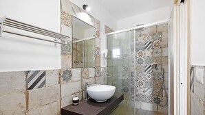 Un baño con un lavamanos blanco, un perchero, una cabina de ducha de vidrio y azulejos estampados.