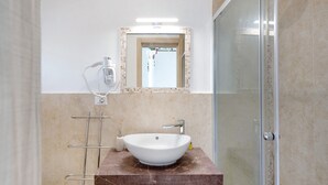 Een badkamer met een witte wasbak, een douchecabine van glas en een spiegel met een betegelde lijst.