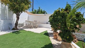 Un espace patio avec un mur blanc, une petite table et des chaises, et une pelouse verte.