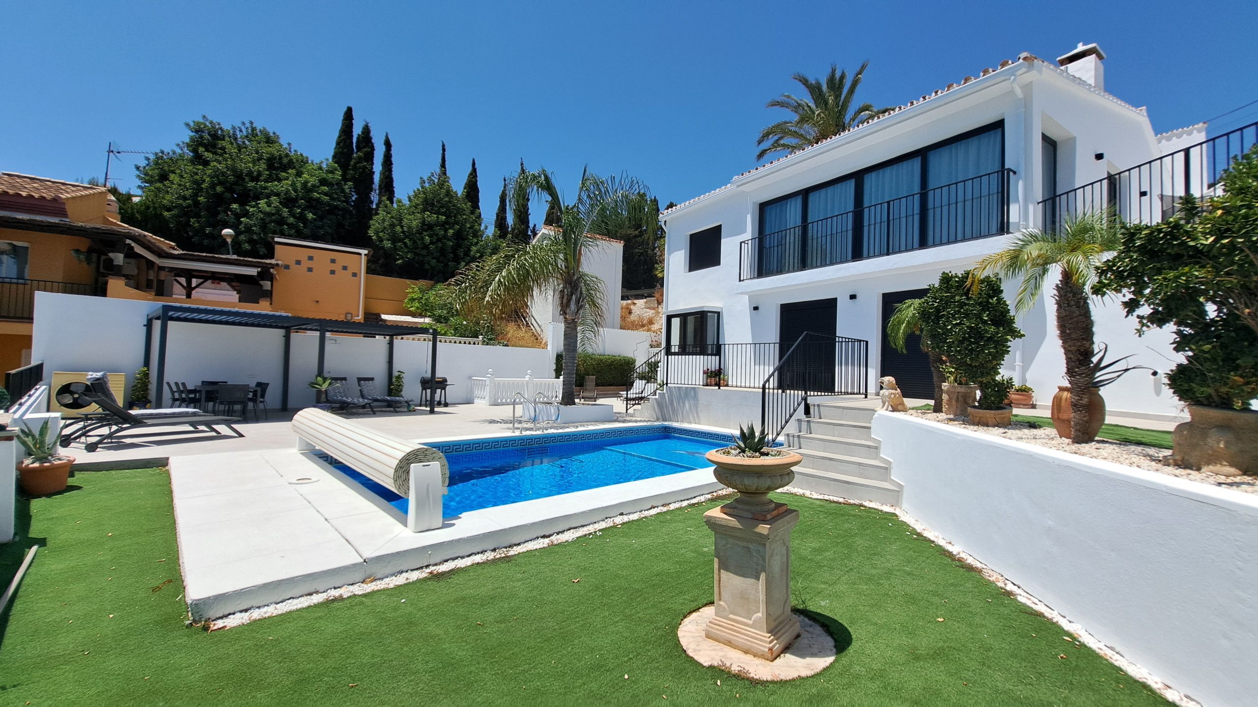 A modern two-story house with a swimming pool, a covered patio, and a well-maintained lawn.