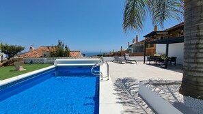 A swimming pool with a clear view of the sea, a patio area with chairs and a table, and a building with a tiled roof in the background. - Ref: 281 Stunning villa with private pool (Fuengirola)