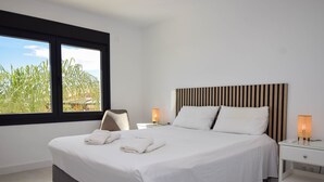 A modern hotel room with a large bed, white linens, a striped headboard, two bedside lamps, and a view of greenery through a window.