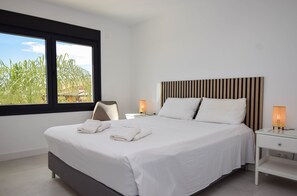 A modern hotel room with a large bed, white linens, a striped headboard, two bedside lamps, and a view of greenery through a window. - Ref: 281 Stunning villa with private pool (Fuengirola)