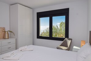 A hotel room with a bed, a chair, a desk, and a window with a view of palm trees.