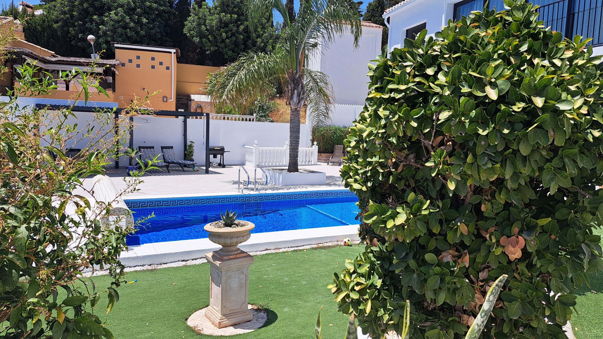 A swimming pool with a geometric tile pattern, surrounded by a white fence, and a palm tree in the background.