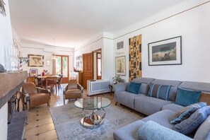 A living room with a sofa, armchairs, a glass coffee table, and a TV.