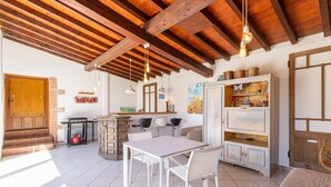 A rustic kitchen with exposed wooden beams, a white table with chairs, and a cabinet with dishes. - Holiday Home 'Lina' with Private Terrace, Wi-Fi and Air Conditioning (Villemolaque)