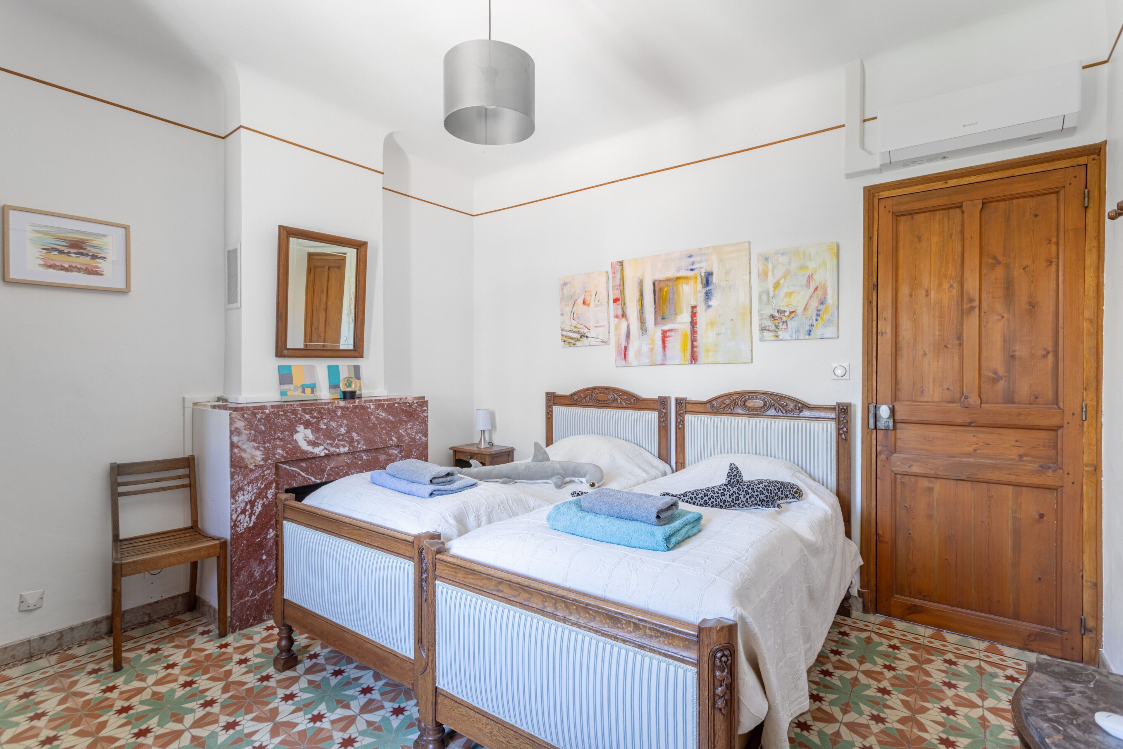 Une chambre avec deux lits, une porte en bois et un sol carrelé.