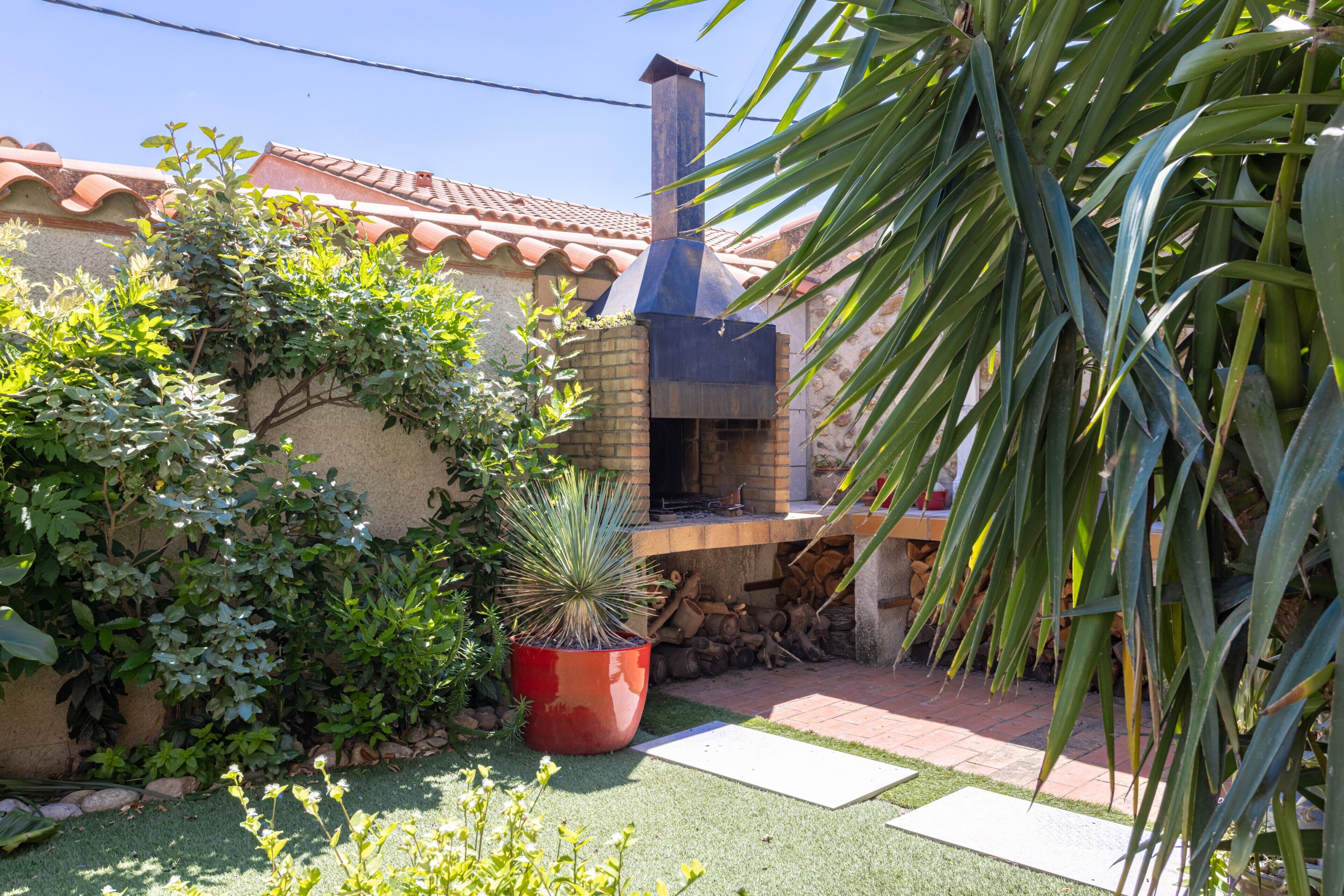 Un horno de ladrillo con chimenea, rodeado de follaje y un tejado de azulejos.