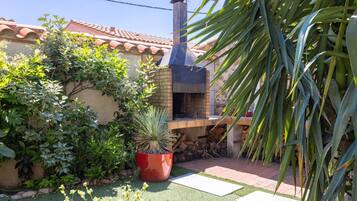 Un horno de ladrillo con chimenea, rodeado de follaje y un tejado de azulejos.