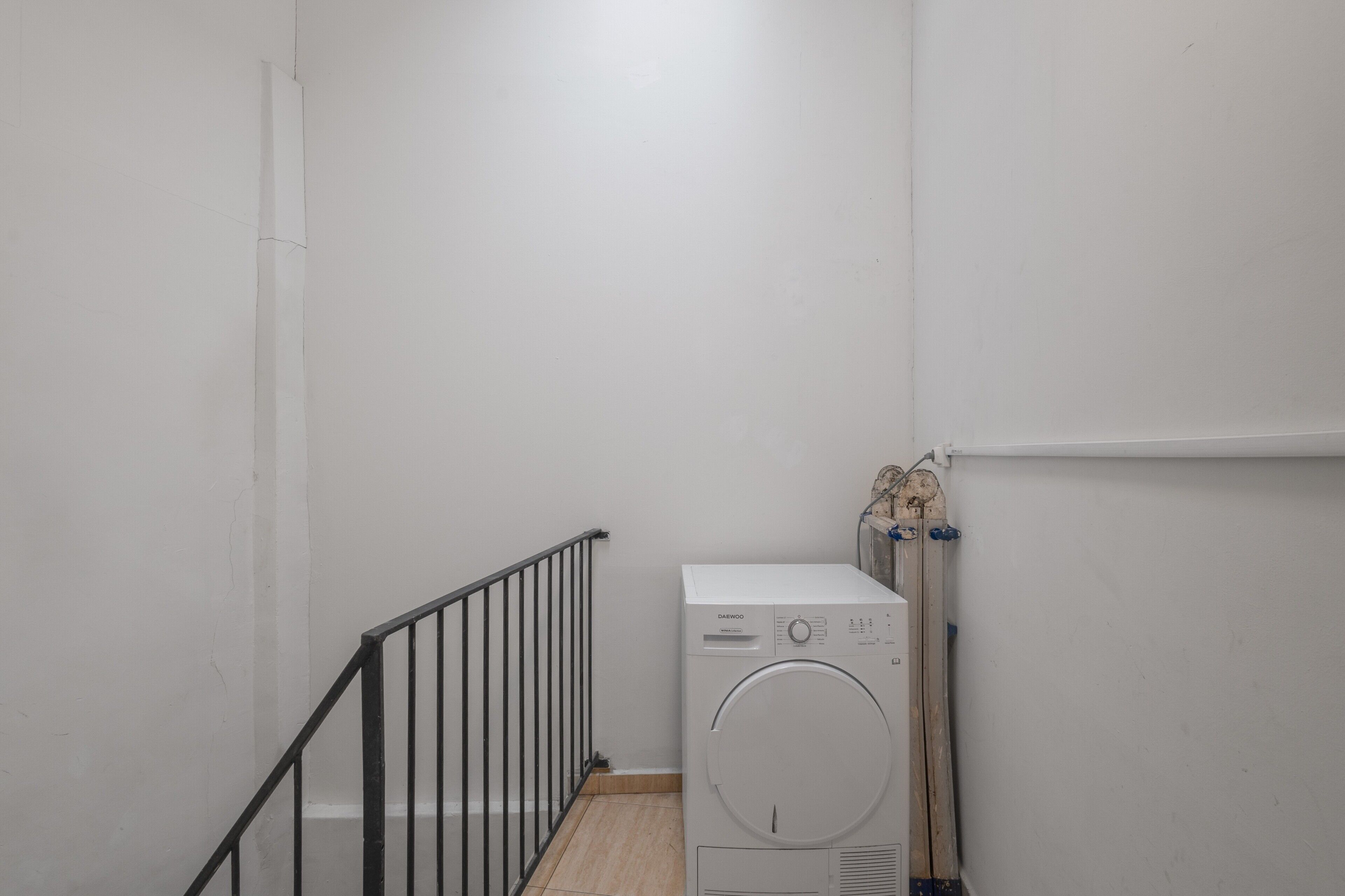 Una sala de lavandería con lavadora, secadora y una barandilla de metal.