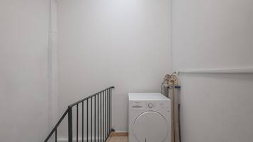 Una sala de lavandería con lavadora, secadora y una barandilla de metal.