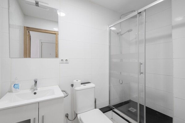 A modern bathroom with a white sink, mirror, toilet, and glass-enclosed shower.