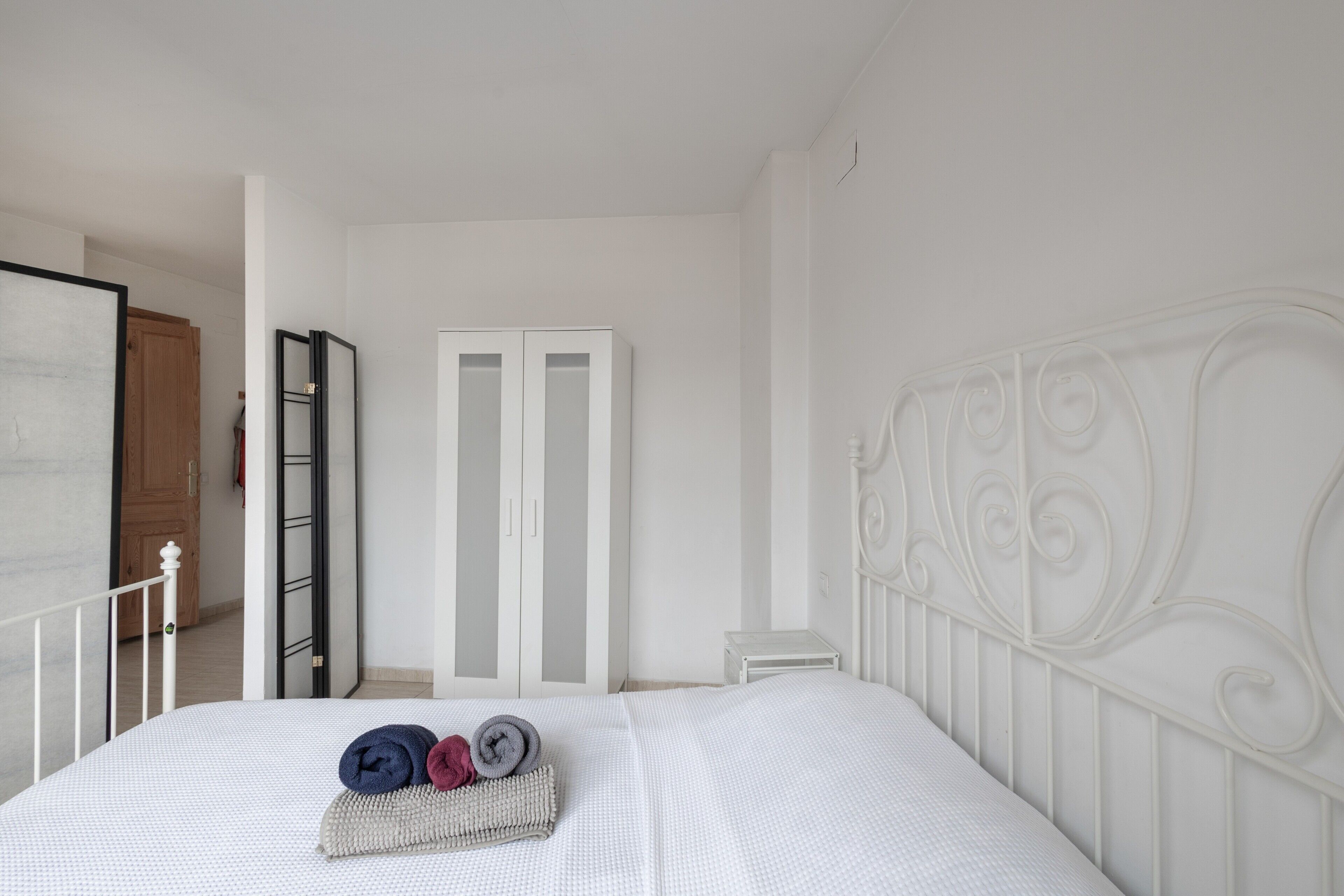 Un dormitorio con cama, armario, una mesita y una puerta que da a otra habitación.