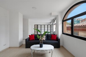 Ein Zimmer mit einer schwarzen Couch, roten Kissen, einem weißen Couchtisch und einer Topfpflanze.