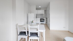 Une cuisine moderne avec des meubles blancs, une table à manger avec des chaises et un petit réfrigérateur.