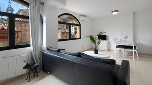 Un salon avec un canapé, une table à manger entourée de chaises, une plante en pot et une vue par la fenêtre.