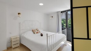 A white bed with a headboard, a small bedside table, two wall-mounted lamps, and a view of greenery outside. - Apartment 'Wonderful Loft Centre' with Balcony, Wi-Fi and Air Conditioning (Manresa)
