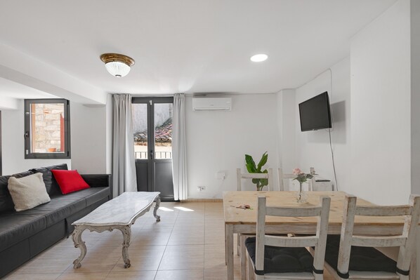 Een moderne woonkamer met een bank, een houten eettafel en een aan de muur bevestigde televisie.