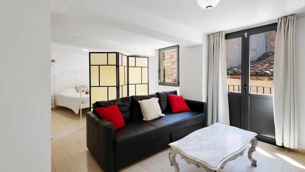 A modern living room with a black leather sofa, a white table, and a sliding glass door leading to an outdoor area. - Apartment 'Wonderful Loft Centre' with Balcony, Wi-Fi and Air Conditioning (Manresa)