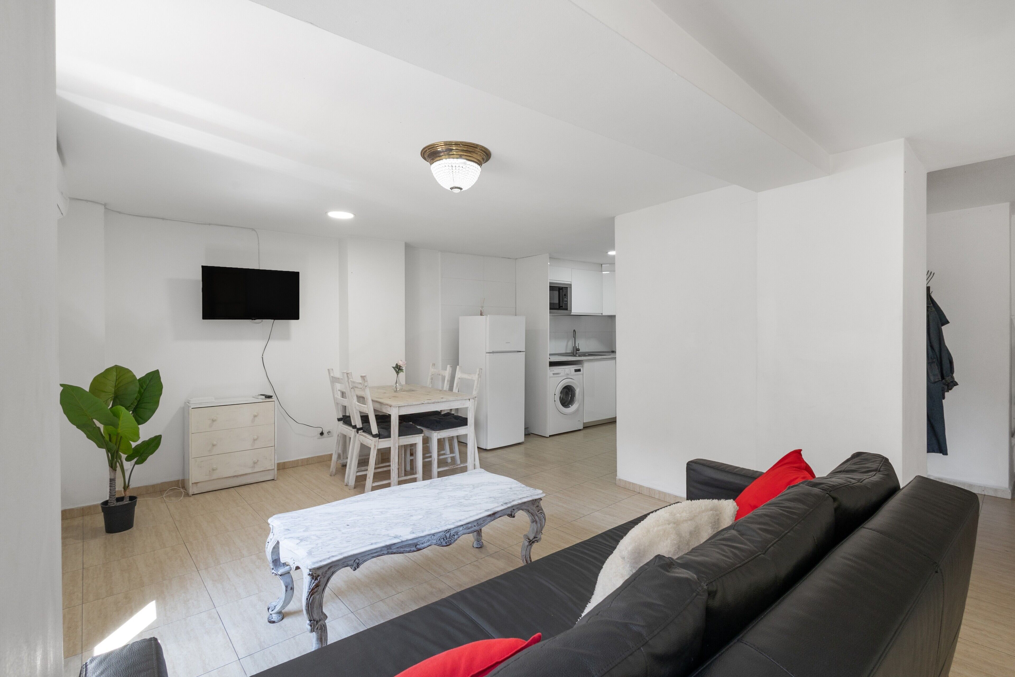A modern living room with a black sofa, a dining table, and a kitchen in the background.