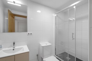 Een moderne badkamer met een wit wastafelmeubel, spiegel, toilet en douchecabine met glazen wanden.