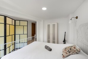 Een slaapkamer met een bed, een wit hoofdbord, een bedlampje, een kledingkast en uitzicht op een balkon met een balustrade.