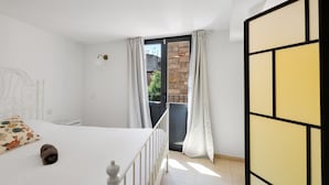 A bedroom with a bed, a white headboard, a small bedside table, a window with curtains, and a view of a stone wall outside. - Apartment 'Wonderful Loft Centre' with Balcony, Wi-Fi and Air Conditioning (Manresa)