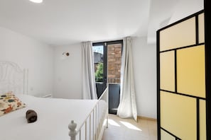 A bedroom with a bed, a white headboard, a small bedside table, a window with curtains, and a view of a stone wall outside. - Apartment 'Wonderful Loft Centre' with Balcony, Wi-Fi and Air Conditioning (Manresa)