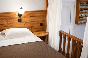 Una cama de madera con cabecera, una mesita de noche, una lámpara de pared y una barandilla de madera.