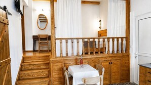 A wooden staircase leading to a balcony with a table and chairs, a wooden cabinet, and a mirror. - Traditional Κefalos Apt with Wooden Ceilings (Kos)