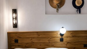 A wooden headboard with a wall-mounted lamp, two white pillows, and two hats on the wall. - Traditional Κefalos Apt with Wooden Ceilings (Kos)