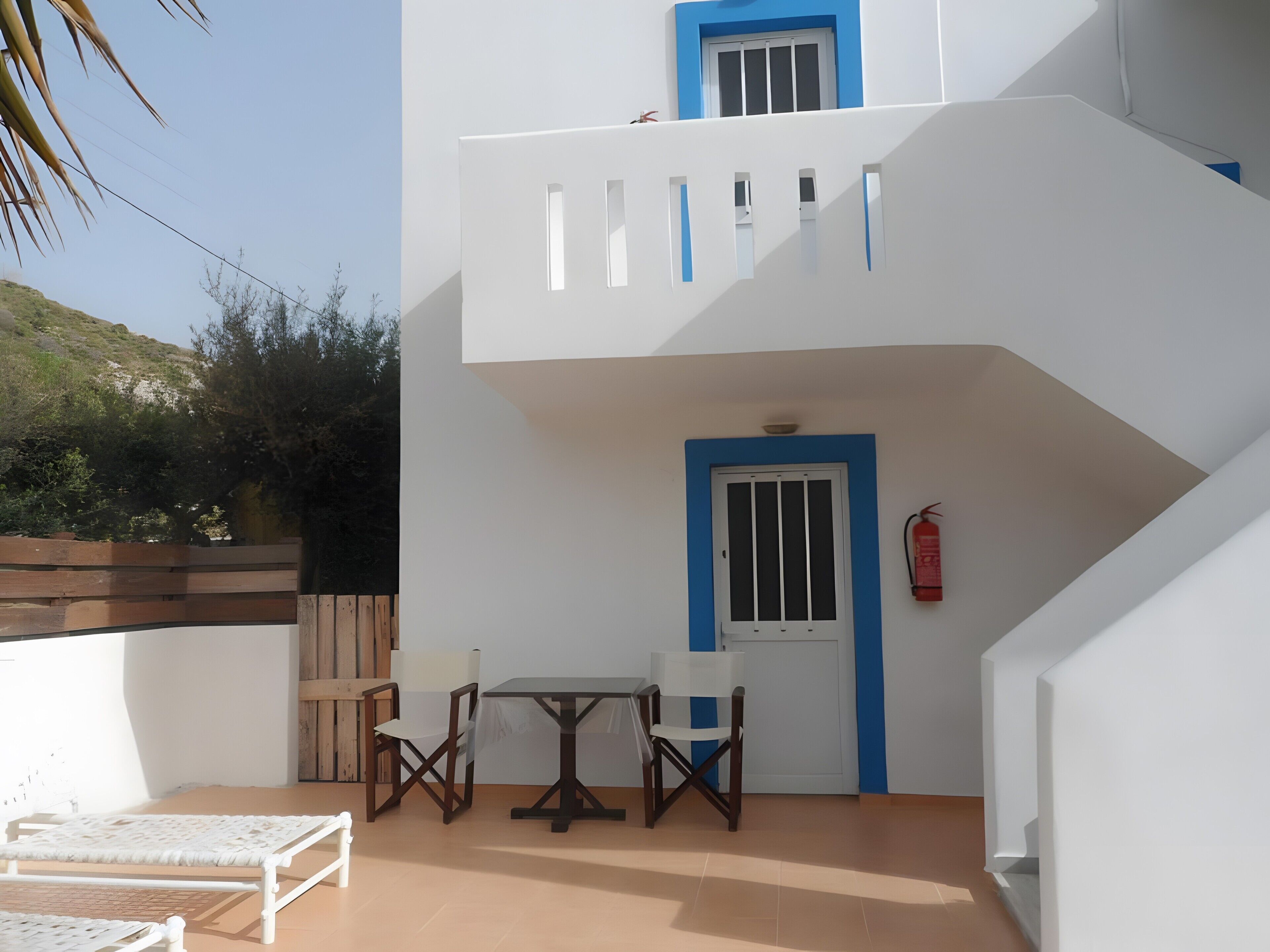 Un bâtiment à deux étages doté d’un balcon, d’une table avec des chaises et d’une porte avec une fenêtre.