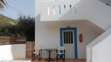 Un bâtiment à deux étages doté d’un balcon, d’une table avec des chaises et d’une porte avec une fenêtre.