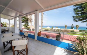 Un espacio al aire libre cubierto con una mesa y sillas, plantas en macetas y vistas al mar.