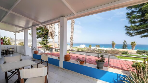 A covered outdoor area with a table and chairs, potted plants, and a view of the sea.