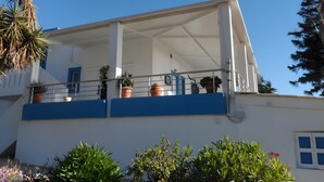 A building with a balcony, potted plants, and a clear blue sky.
