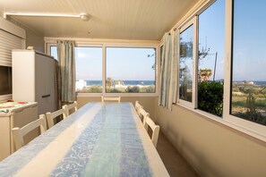 Un comedor con mesa y sillas, ventanas amplias, un refrigerador y vista al mar.
